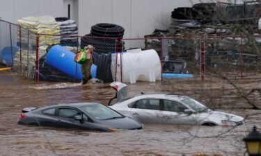 A man wearing chest waders walks past cars abandoned in floodwaters in a mall parking lot in Halifax