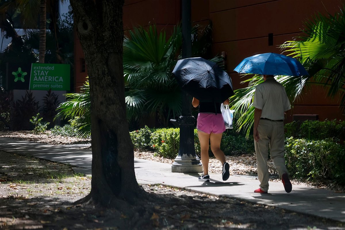 <i>Eva Marie Uzcategui/Bloomberg/Getty Images</i><br/>Pedestrians carry umbrellas during a heat wave in Miami