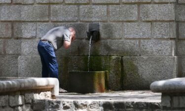 A man refreshes his face in a public fountain on July 11