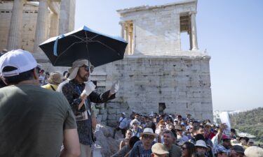 A tour guide uses an umbrella and gloves to shield himself from the sun while working at the Acropolis archaeological site during extreme hot weather in Athens