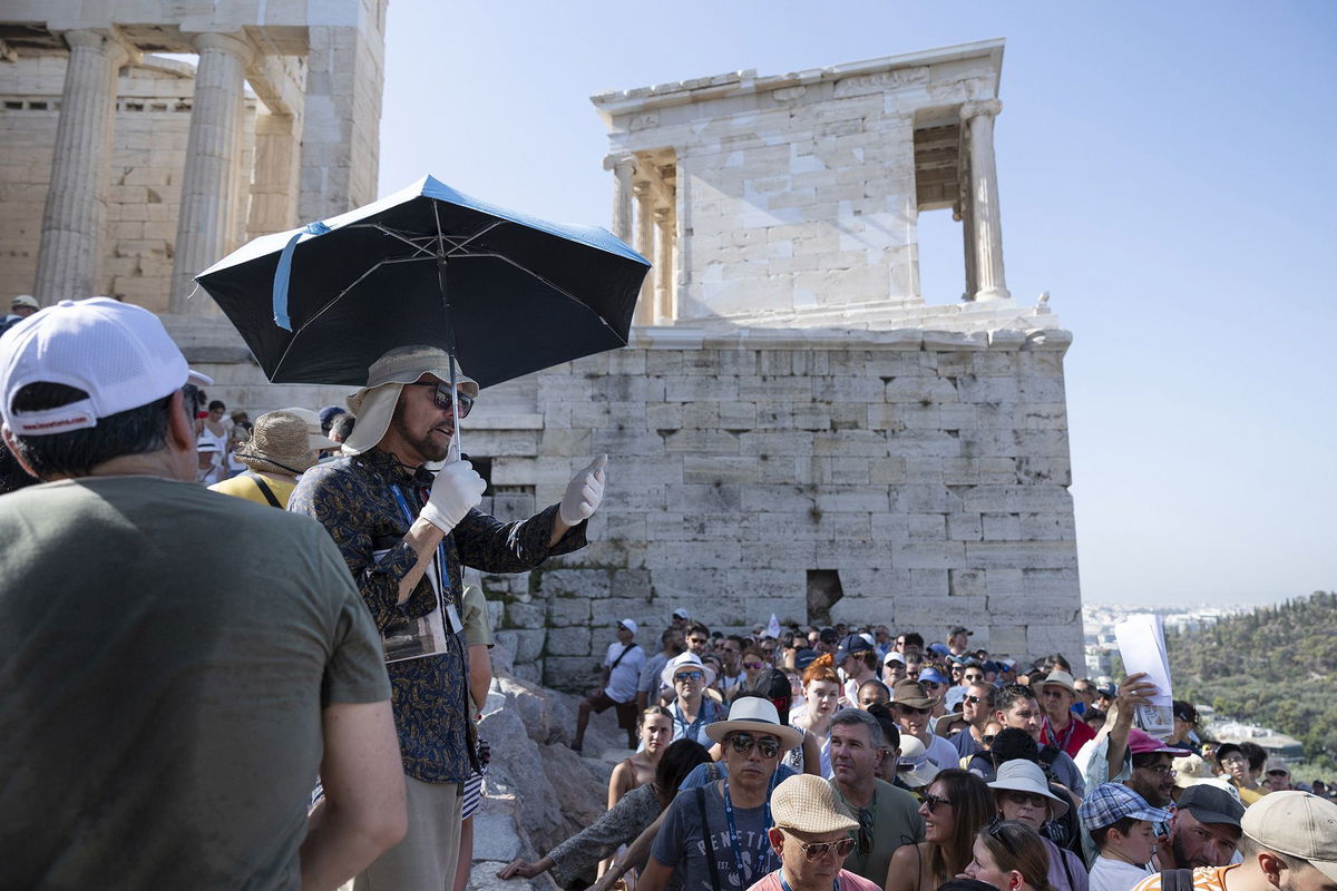 <i>Yorgos Karahalis/Bloomberg/Getty Images</i><br/>A tour guide uses an umbrella and gloves to shield himself from the sun while working at the Acropolis archaeological site during extreme hot weather in Athens