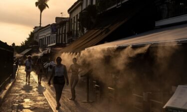 People walk next to a mist machine to cool down