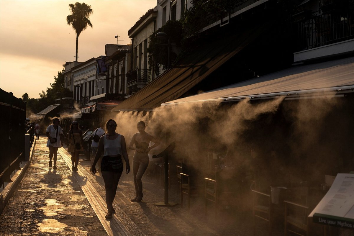 <i>Petros Giannakouris/AP</i><br/>People walk next to a mist machine to cool down