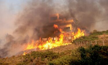 Flames engulf a house as a wildfire burns in Saronida