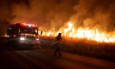 A firefighter watches flames from the Rabbit Fire approach Gilman Springs Road late Friday