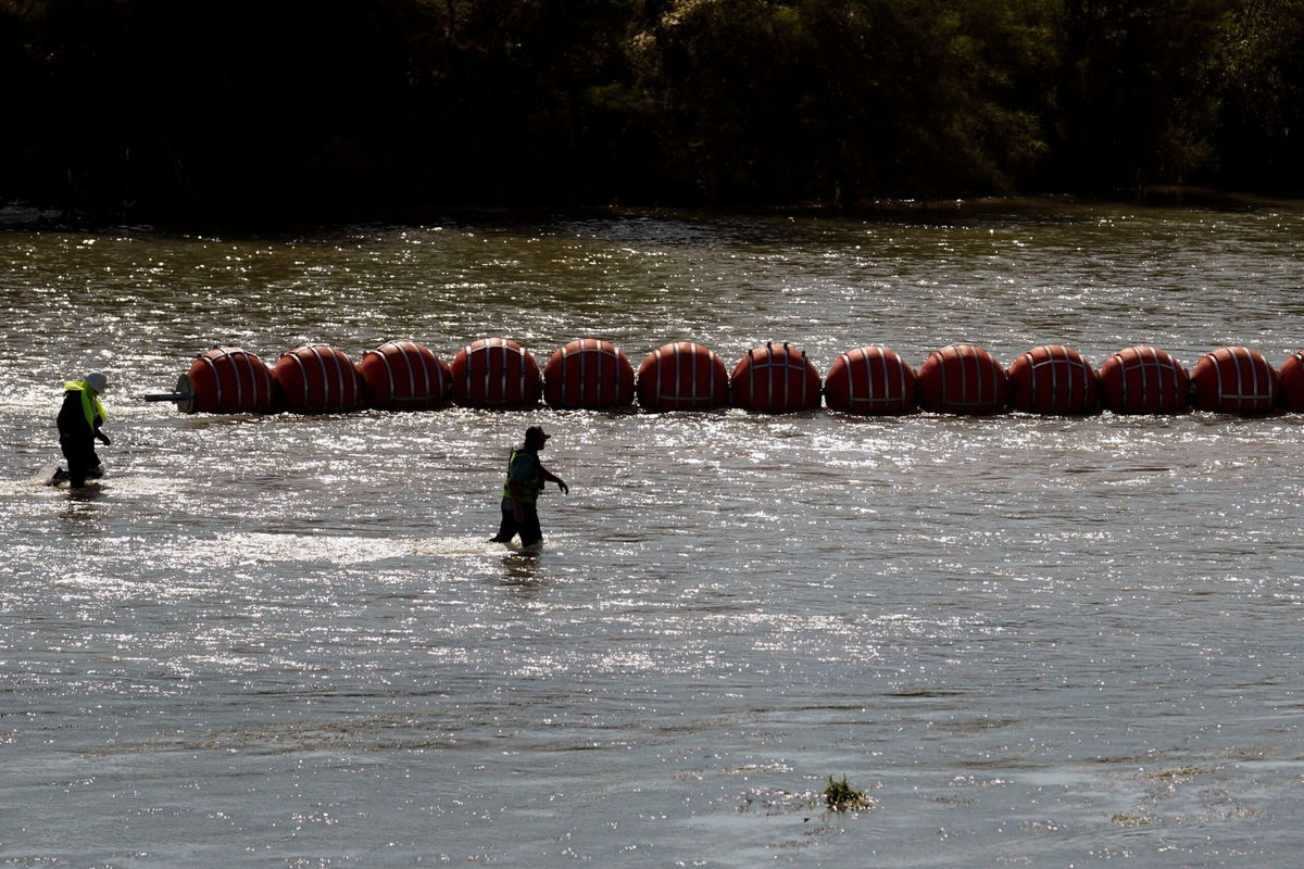 <i>Eric Gay/AP</i><br/>Workers help deploy a string of large buoys to be used as a border barrier at the center of the Rio Grande near Eagle Pass