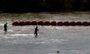 Workers help deploy a string of large buoys to be used as a border barrier at the center of the Rio Grande near Eagle Pass