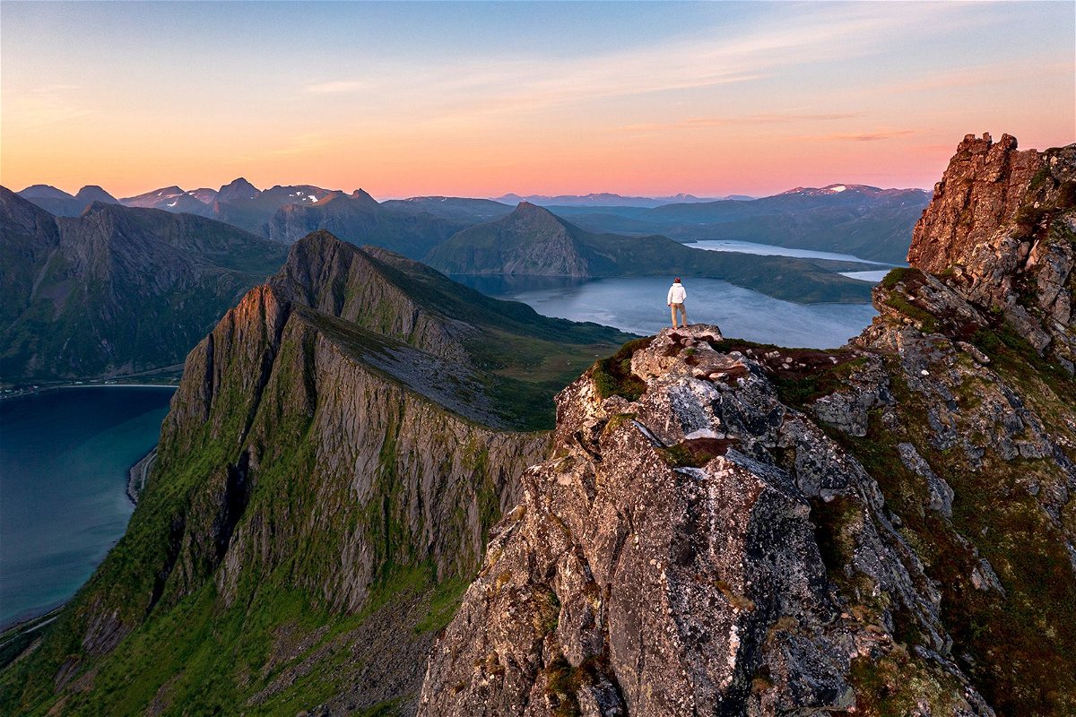 A man is pictured watching sunrise while standing on Husfjellet mountain peak on Senja Island in Norway.	