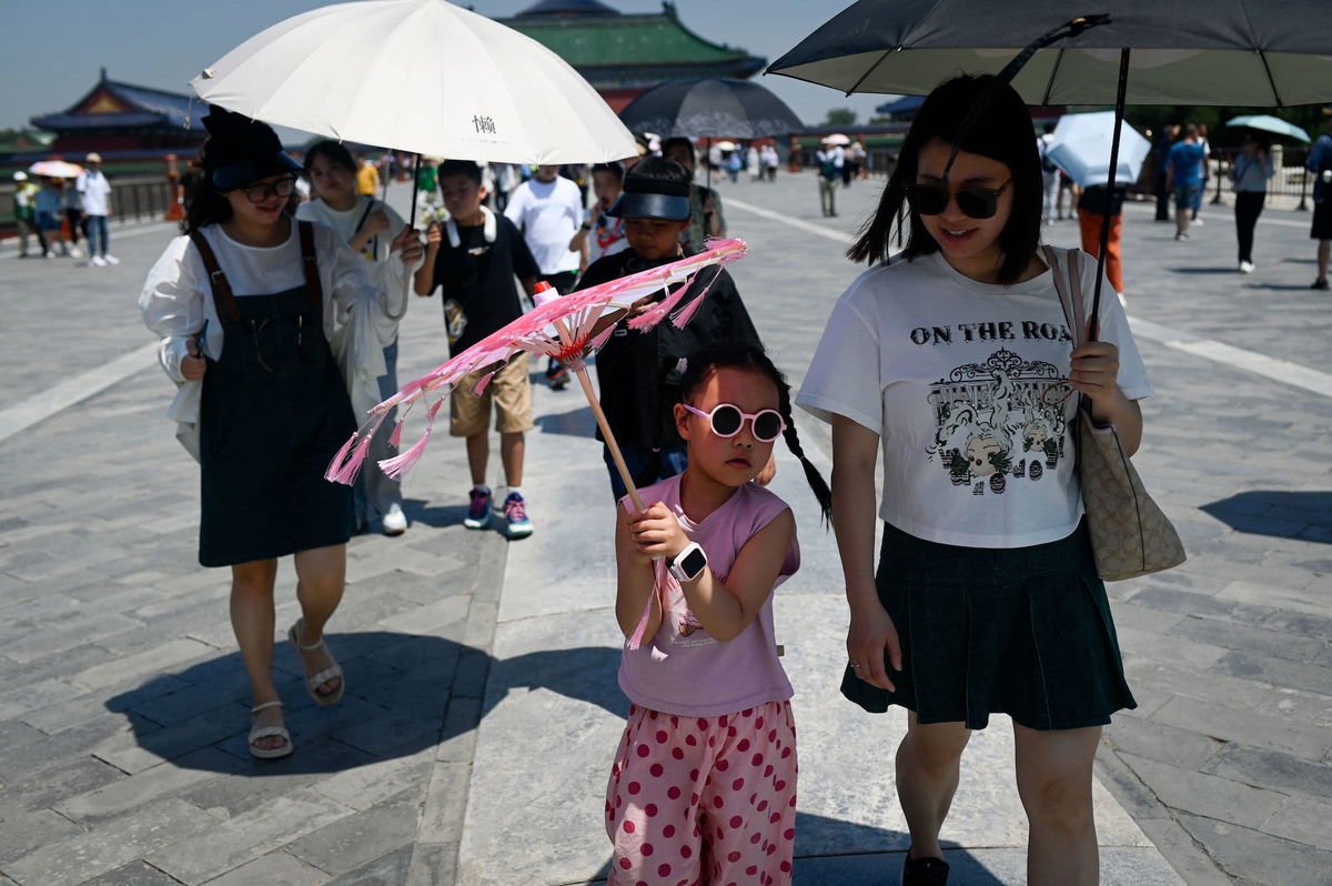 Tourists use umbrellas to shelter from the sun on a hot day in Beijing on June 30.