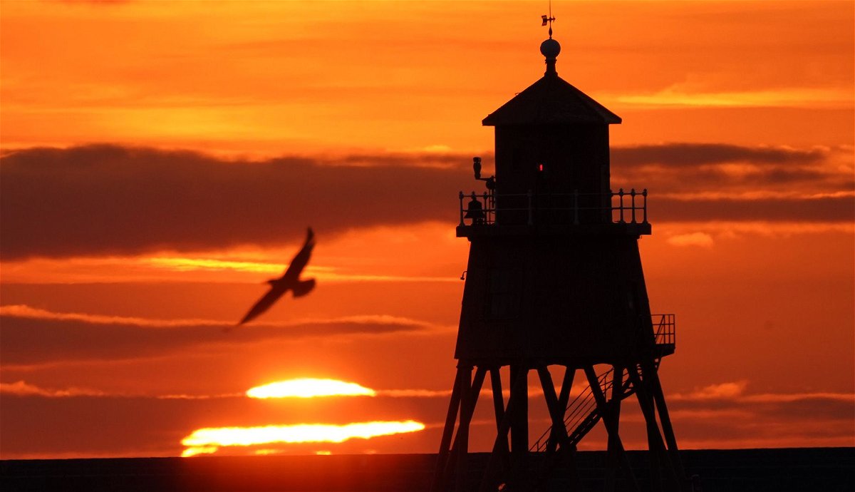 A pumpkin-colored sunrise emerges during the fall equinox 2021 at England's Herd Groyne Lighthouse, which stands guard at the mouth of the River Tyne near the North Sea.