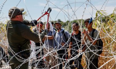 A border patrol agent cuts razor wire to allow migrants who've been waiting in the sun for hours