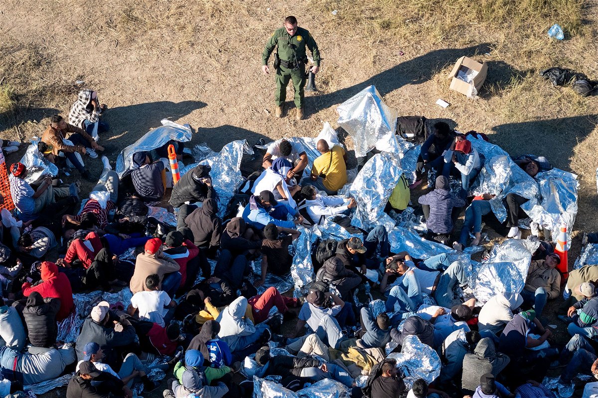 <i>John Moore/Getty Images</i><br/>A US Border Patrol agent speaks with immigrants waiting to be processed after crossing from Mexico into the United States on December 17