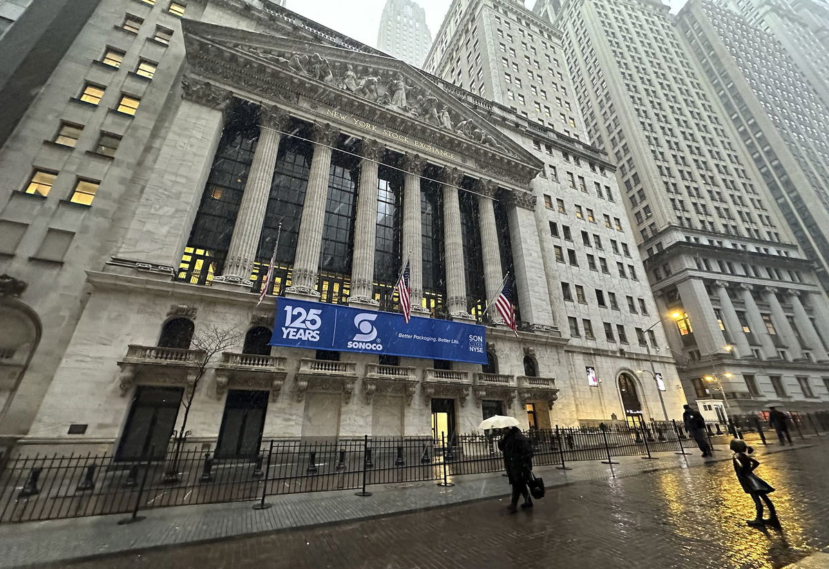 Pedestrians pass the New York Stock Exchange as snow falls on Tuesday, February 13, 2024 in New York.