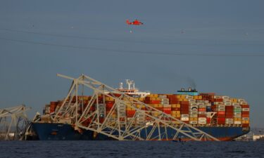 A helicopter flies over the Dali cargo vessel and the wreckage of the Francis Scott Key Bridge.