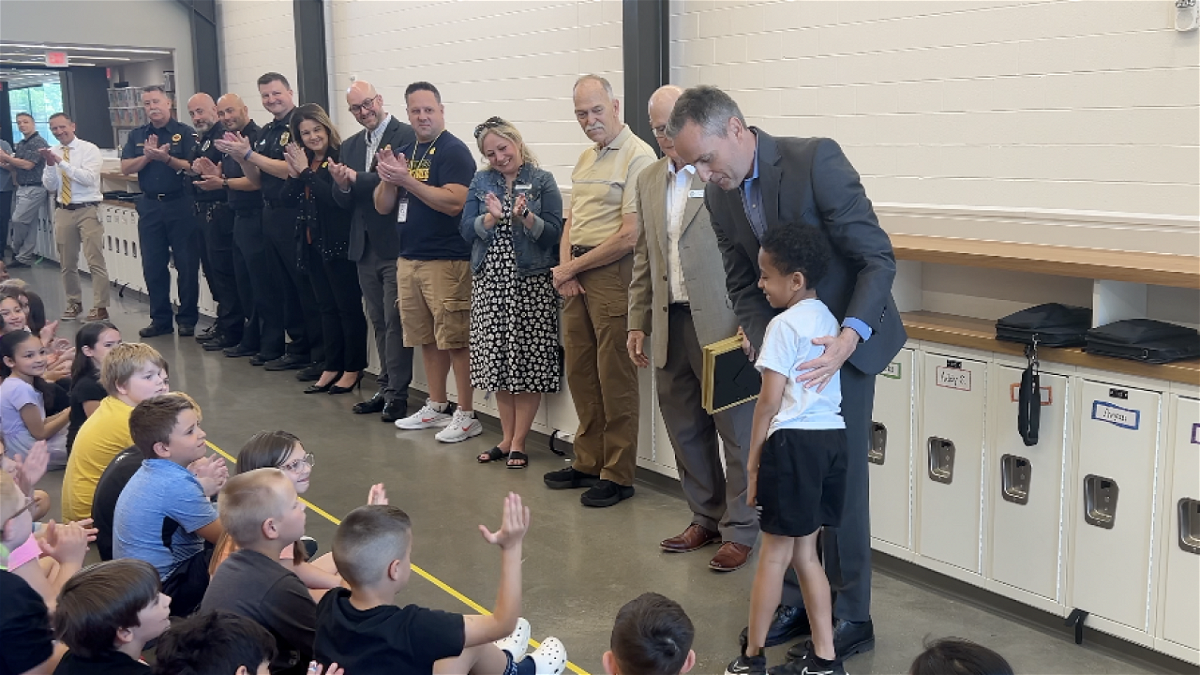 Superintendent Steve Wood congratulates second grader Trey Lewis for alerting others when a classmate had a severe allergic reaction to a granola bar.
