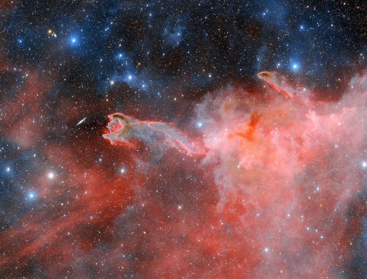 A cometary globule, named CG 4, is the cosmic phenomenon that resembles a ghostly hand seemingly reaching toward a spiral galaxy in a new image taken by the Dark Energy Camera.