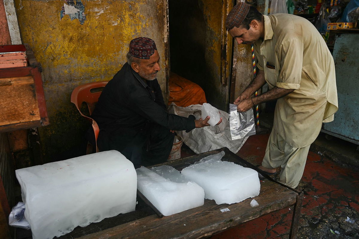 A vendor selling ice, slices a piece from an ice block for a customer at his shop on a hot summer noon in in Karachi on May 27.