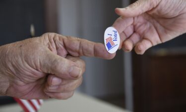 Poll worker Kenny Smith hands a sticker to a voter on Super Tuesday in Stillwater