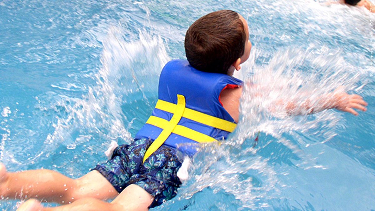 Child wearing life jacket and swimming