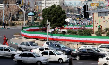 Cars drive past a wall covered by a banner in the colours of the national flag in Tehran