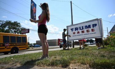 Julianna Grooms holds a photo of former President Donald Trump as neighbors help she and her mother secure a Trump yard sign that they used tape to add the name of Trump's running mate J.D. Vance outside their home on July 16