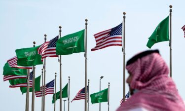 A man stands under American and Saudi Arabian flags at a square in Jeddah