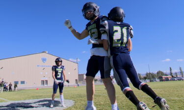 Two football players bump shoulders in mid-air before a game.