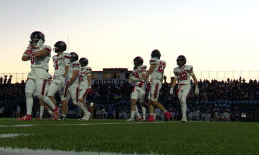 Football players walk towards their respective sidelines at sunset.