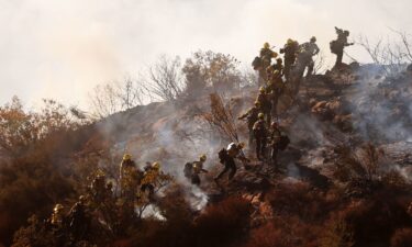 Firefighters work as the Franklin Fire burns near a building on Tuesday in Malibu