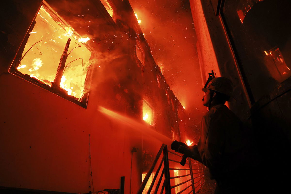 <i>Etienne Laurent/AP via CNN Newsource</i><br/>A firefighter works from a deck as the Palisades Fire burns a beach front property in Malibu on January 8.